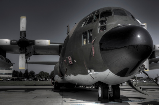 An HDR shot of a Lockheed C130H Hercules military transport aircraft, its polished radome/nosecone reflecting the sun and concrete.
