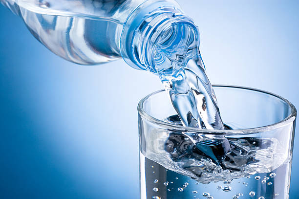 wasser aus der flasche ins glas auf blauem hintergrund gießen - destilliertes wasser stock-fotos und bilder