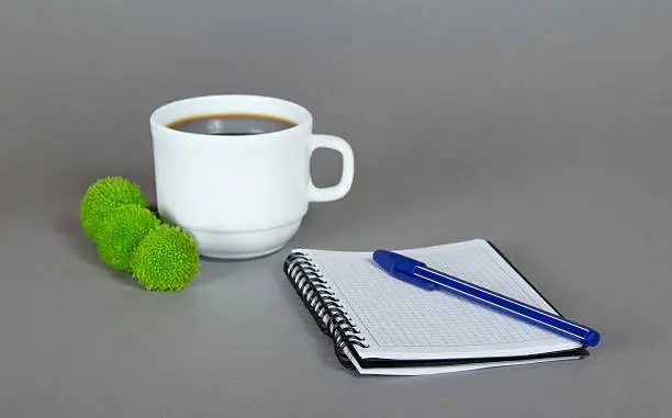 Cup of fragrant coffee, green chrysanthemums, a sketchpad and a ballpoint on a gray background