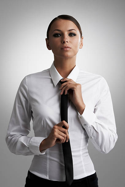 She's ready for business A beautiful young woman straightening her tie while looking at the camera woman necktie stock pictures, royalty-free photos & images