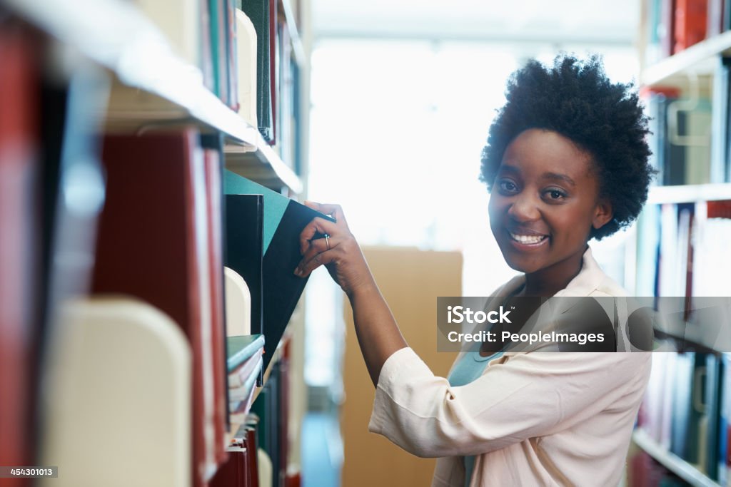 Working on her thesis A young woman selecting some books in the library Dissertation Stock Photo