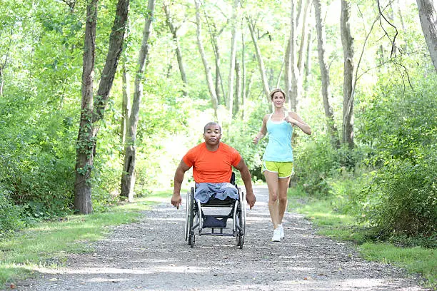 woman jogging behind man in wheelchair on outdoor trail