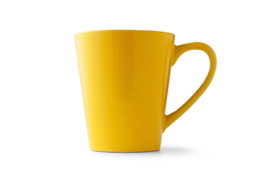 Low angle view of a yellow ceramic or pottery cup with handle standing sideways on a white background