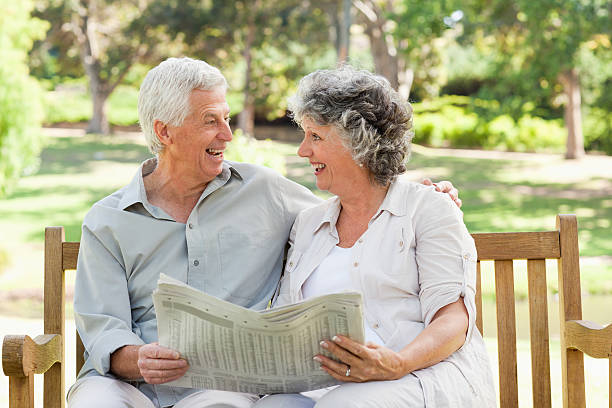istock elderly couple sitting on a bench holding newspaper and laughing 454325037