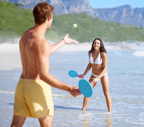 They are always active A happy young couple playing tennis on the beach together together paddle ball stock pictures, royalty-free photos & images