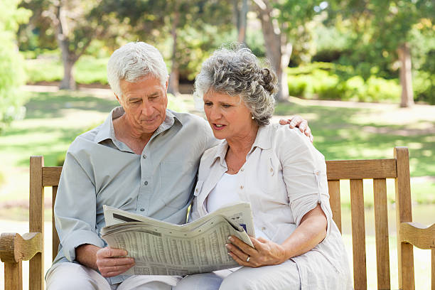 istock Elderly couple reading newspaper on a park bench 454326387