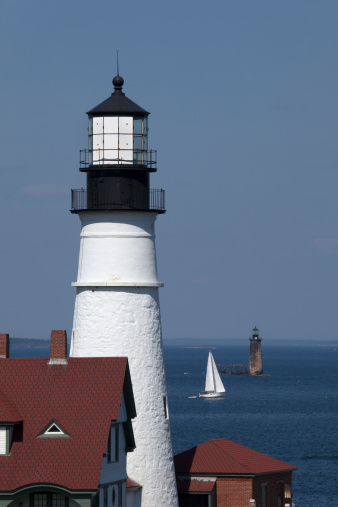 At low tide, a sail boat cruises by the Portland Head Lighthouse and the Spring Point Light in the Portland Harbor, part of the Casco Bay, Portland, Maine.