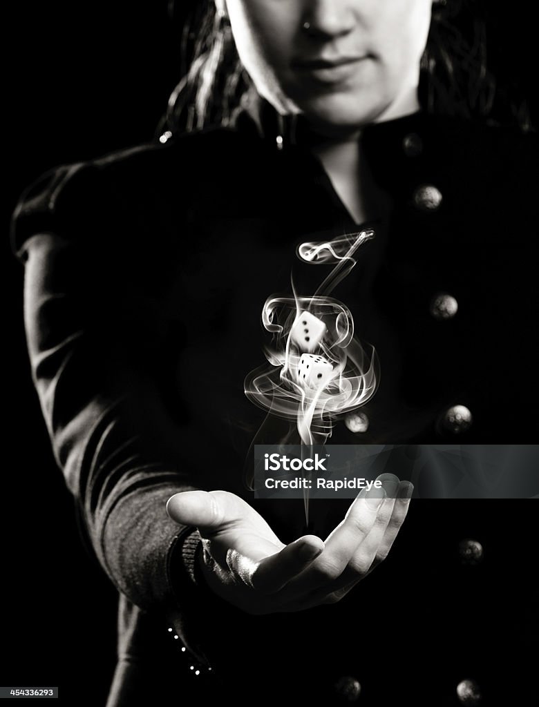 Woman tosses dice in smoke swirl: luck is a toss-up! Concept black and white shot of a young woman tossing up dice in a swirl of smoke. Good or bad fortune, it's a toss-up or the luck of the throw, and your dreams might go up in smoke! Dice Stock Photo