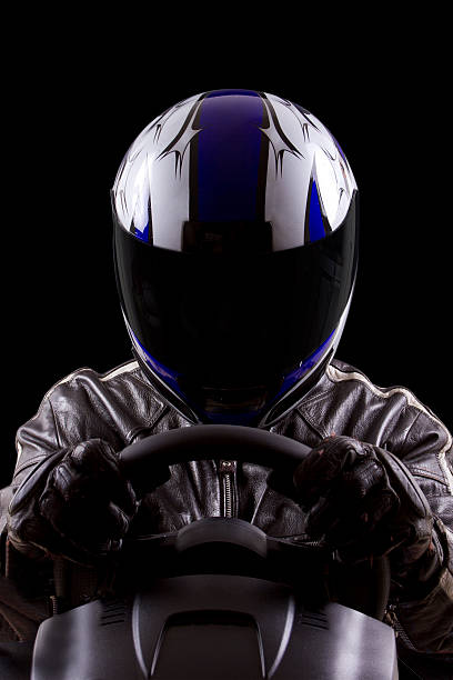 Racer Wearing a Helmet and Leather Protective Gear racerwearing leather racing suit and blue helmet on a steering wheel Helmet stock pictures, royalty-free photos & images