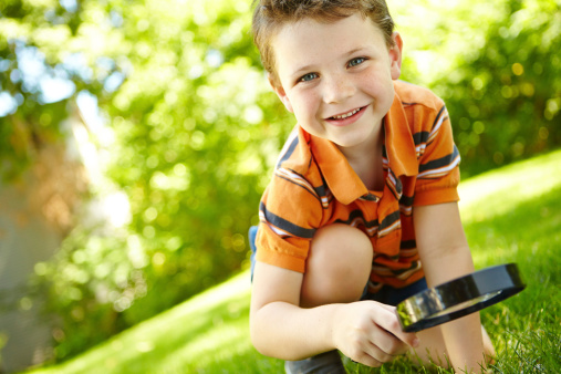 Cute little boy spending time outdoors and using a magnifying glass