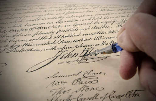 Close-up of some of the  signatures on the Declaration of Independence made to look like it is being signed with an antique administrative pen.