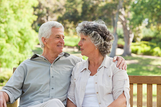istock Elderly couple sitting on bench smiling at each other 454354069