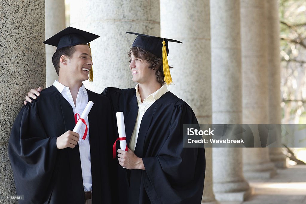 Dois-formados homens segurando seu diploma enquanto sorrindo para cada - Foto de stock de 20 Anos royalty-free