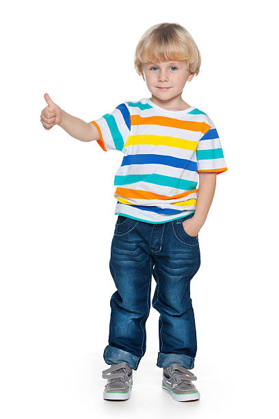 A joyful fashion little boy holds his thumb up on the white background