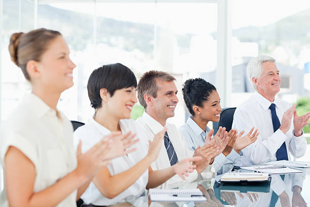 istock Side view of applauding businesspeople sitting at a table 454384789