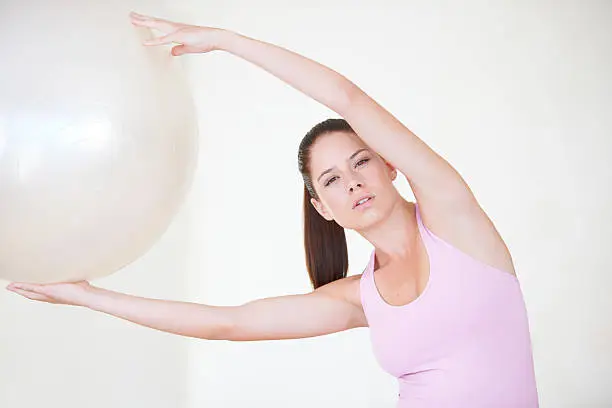 Shot of a young woman with her arms stretched above her head holding an exercise ball