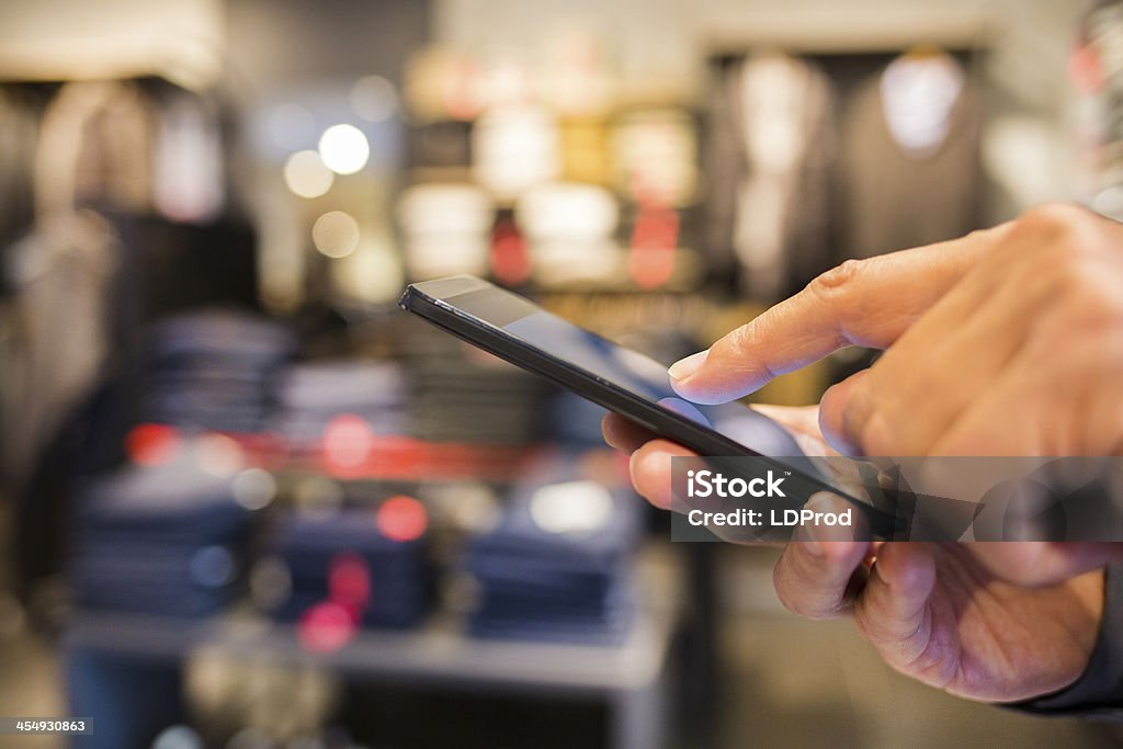 Man using mobile  phone in clothing store Male smart phone hand digital sms shop background Adult Stock Photo