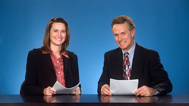 Smilng newcasters. Male and female newcasters sitting at desk smiling at viewer. newscaster stock pictures, royalty-free photos & images
