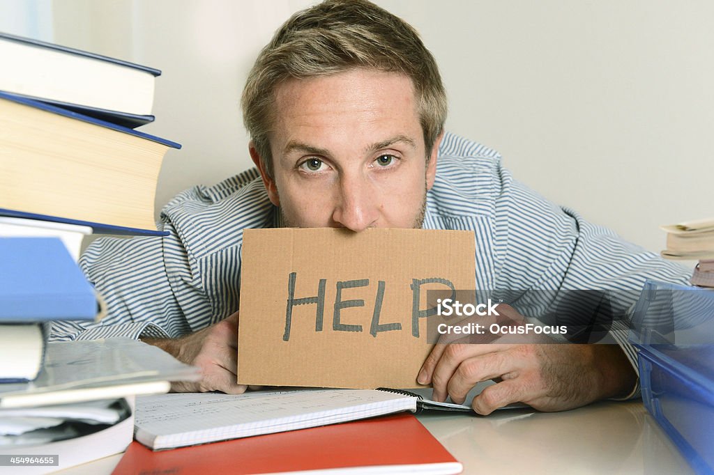 Young man with piles of book and a cardboard help sign Young Student Stressed and Overwhelmed asking for Help Book Stock Photo