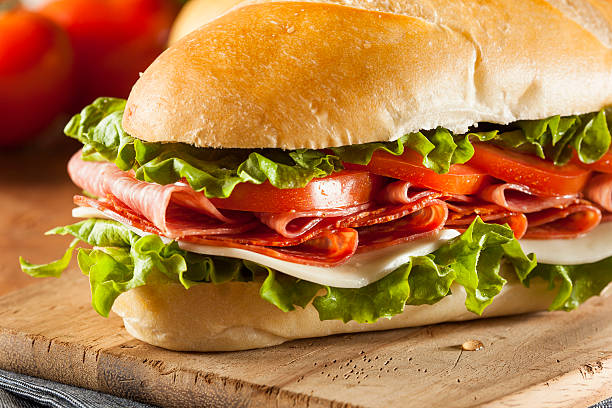 Close-up Italian sub hoagie sandwich cutting board stuffed Homemade Italian Sub Sandwich with Salami, Tomato, and Lettuce submarine sandwich photos stock pictures, royalty-free photos & images