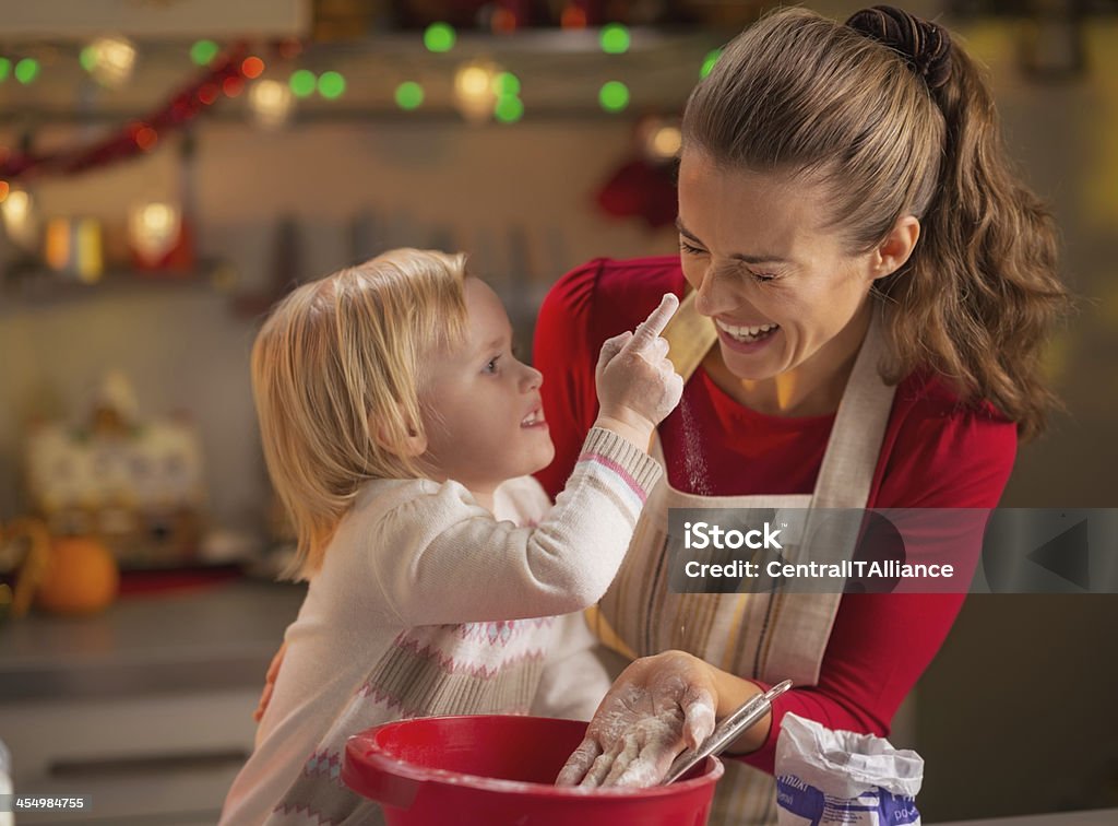 Baby trying to smear mothers nose with flour in kitchen Baby trying to smear mothers nose with flour while making christmas cookies Flour Stock Photo