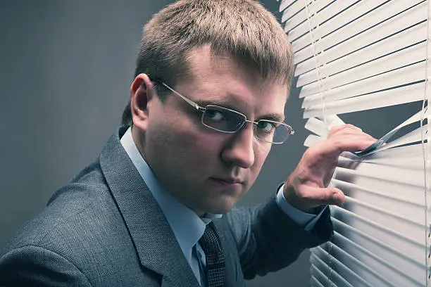 A young man looking through window blinds