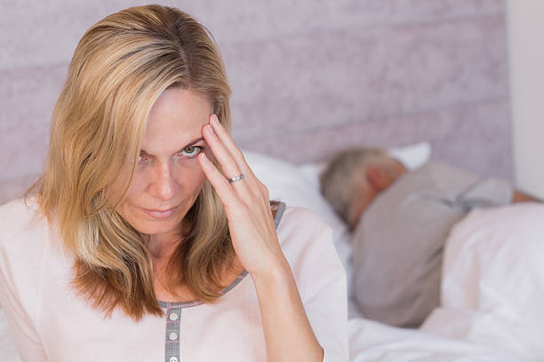 istock Frowning woman with a headache while her husband is sleeping 454997935