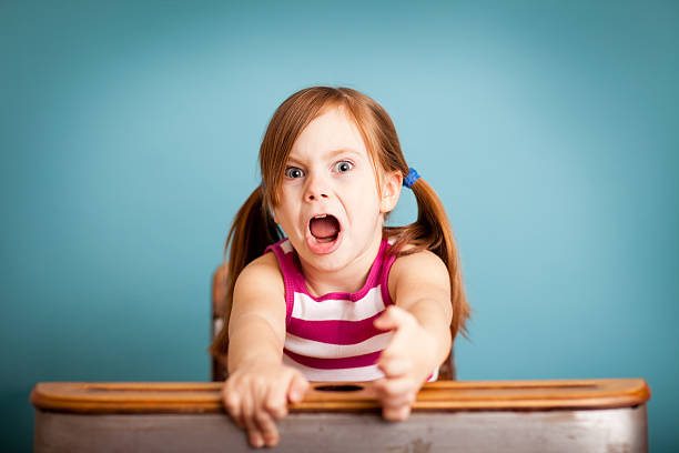 Angry/Uncooperative Young Girl Sitting at School Desk stock photo