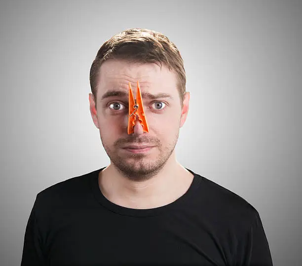 Portrait of caucasian man with orange clothespin on his nose - bad smell concept photography. 