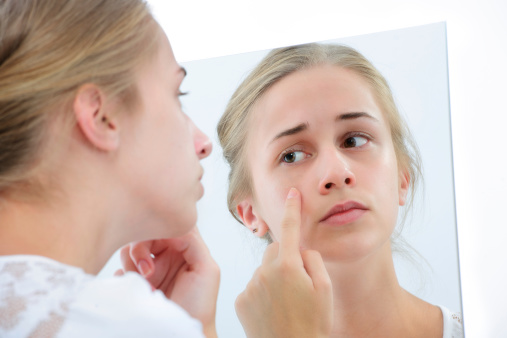 Teenage girl checking her face for pimple in the mirror