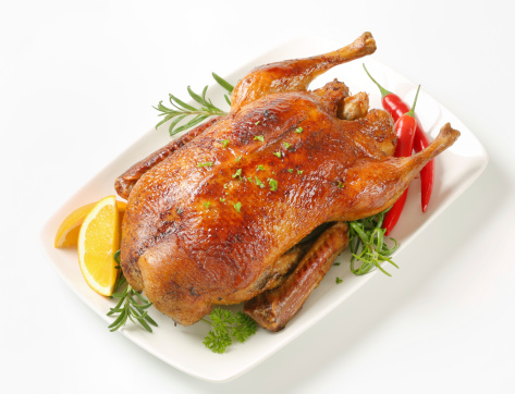 whole roasted duck garnished with herbs and vegetables on white plate