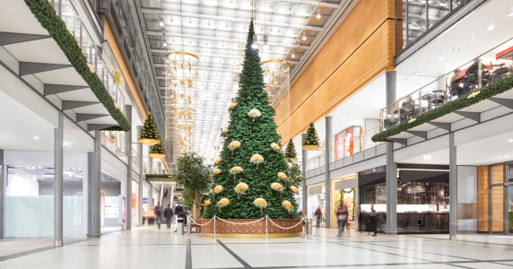 Inside images of a shopping mall with a big Christmas tree and decorations. Shoppers are walking around, browsing and buying holiday gifts.