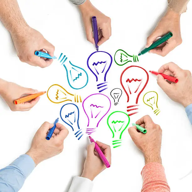 Photo of Seven hands drawing multicolored lightbulbs