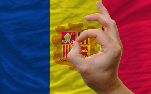 man showing excellence or ok gesture in front of complete wavy andorra national flag of  symbolizing best quality, positivity and succes