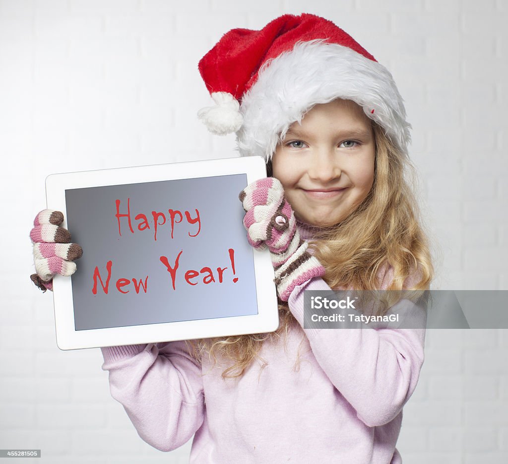 Girl in Santa hat holding tablet reading Happy New Year  Child in christmas hat with tablet pc. Happy girl showing tablet screen 6-7 Years Stock Photo