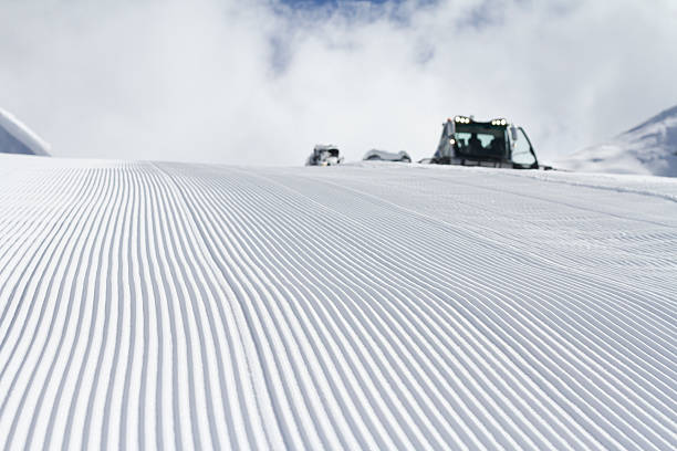Close-up straight line rows of freshly prepared groomed ski slope piste with bright shining sun and clear blue sky background. Snowcapped mountain downhill landscape at europe winter skiing resort