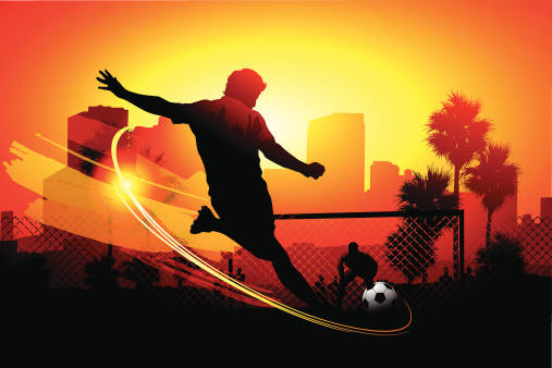 EPS 10 vector silhouette of a street soccer scene with a player winding up for a shot with the goalie guarding the goal post in the background.