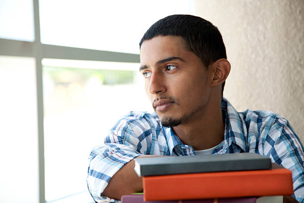 Hispanic student Hispanic student thinking. He is a student and has a stack of books in front of him. puerto rican ethnicity stock pictures, royalty-free photos & images