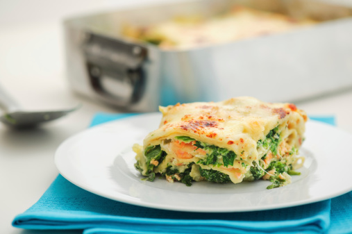 A plate with a nice piece of salmon lasagna with spinach leaves. Selective focus shallow depth of field on a clean, white background.