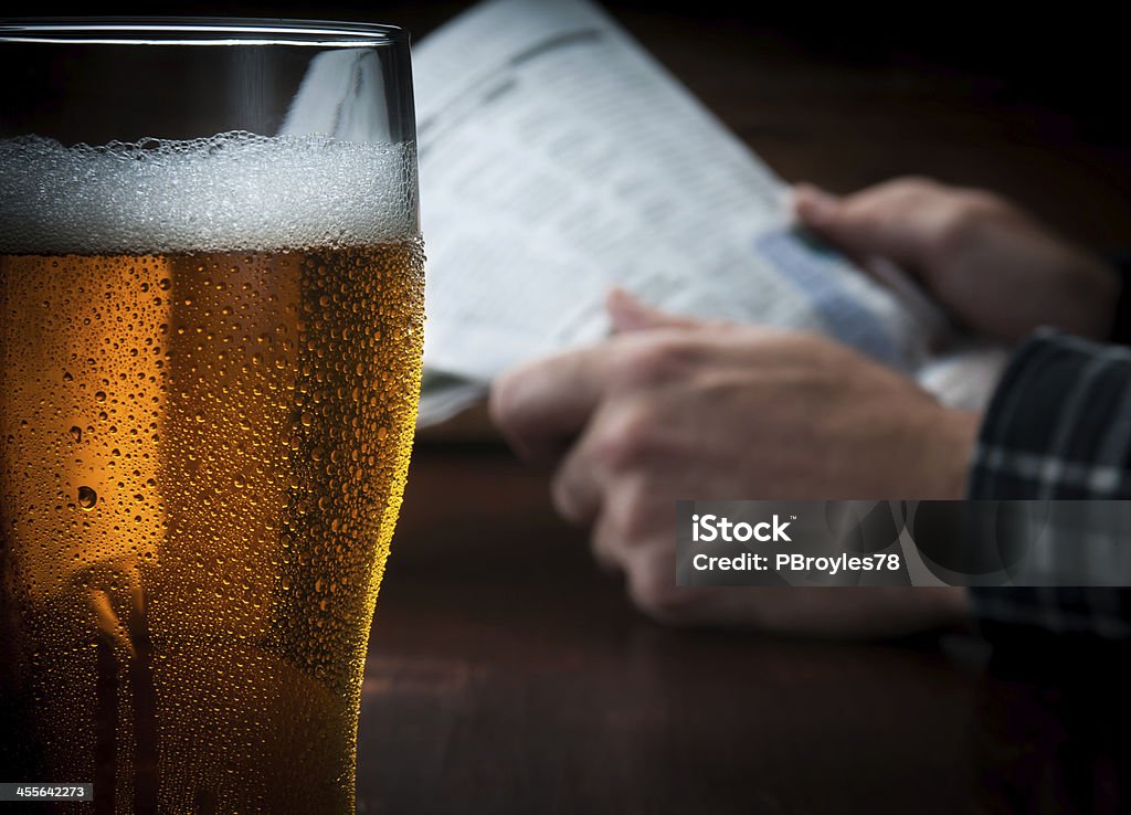 Cold Beer with Casual Background Cold beer with person reading newspaper in the background. Beer - Alcohol Stock Photo