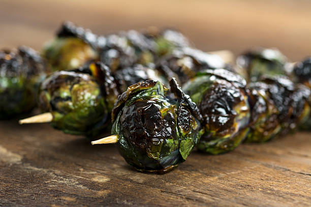Charred grilled purple Brussel sprout kabobs on a wood table stock photo