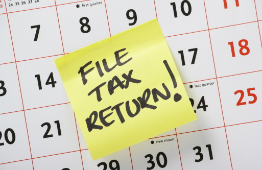 Hand written reminder to File Tax Return on a yellow post it note stuck to a calendar background