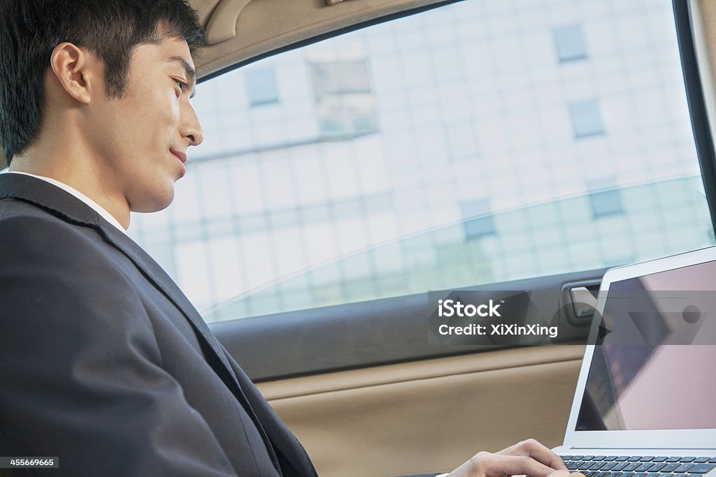 Businessman in Back Seat of Car Typing on Laptop Businessman in Back Seat of Car Typing on Laptop, Low Angle View Car Interior Stock Photo