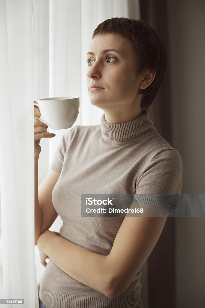 Charming Pretty woman drinking coffee Charming Pretty woman drinking coffee by the window Adult Stock Photo