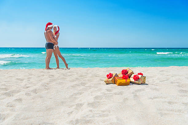 küssen paar in santa hüte am strand mit geschenk-boxen - gift new year couple men stock-fotos und bilder