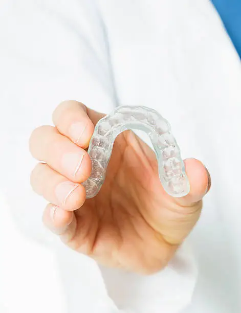 A dentist holding a dental mouthguard in his hand.