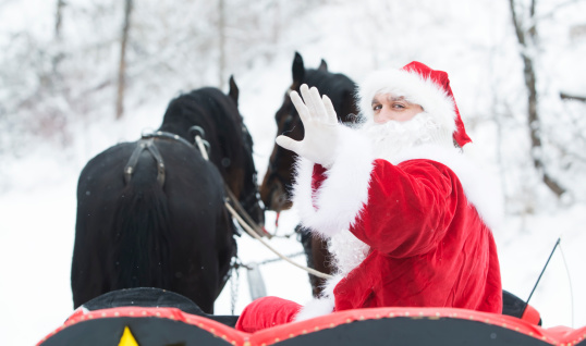 Santa Claus waving in a sleigh pulled by horses