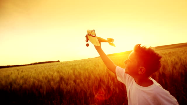 Young boy dreams about being a pilot as he is flying his airplane at sunset.  The sense of freedom and joy that he displays is very attractive.  A feeling of well being and a healthy lifestyle are what this clips is all about.  The warm golden scene exudes an emotional joy about life and living in the countryside.   A bumper crop of wheat makes for a good background adding to a feeling of dreaming.
