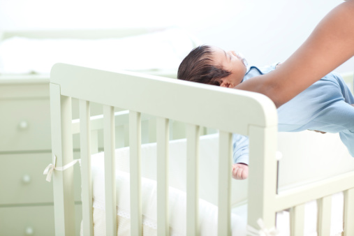 A mother putting her baby to sleep in his cradle.