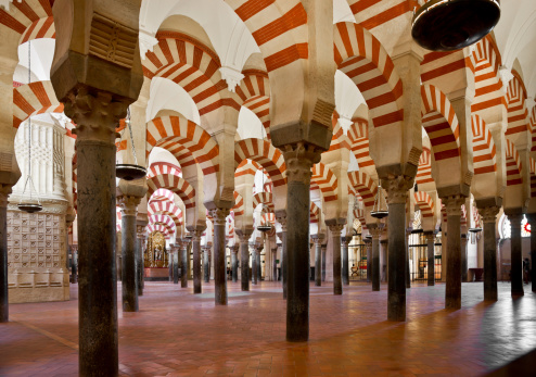 Interior of La Mezquita Cathedral (Mosque of Cordoba) in Córdoba, Spain. More than 850 columns of granite, onyx, jasper and marble support the roof. The double arches consist of a lower horseshoe arch and an upper semi-circular arch. The famous alternating red and white voussoirs of the arches were inspired by those in the Dome of the Rock. This photograph depicts columns in the part of the mosque that was built by Al-Mansur Ibn Abi Aamir in 987.